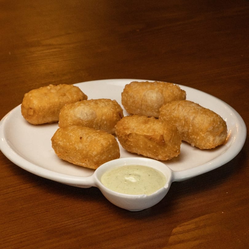 Six golden-brown Colombian empanadas on a white plate with a side of creamy green dipping sauce.