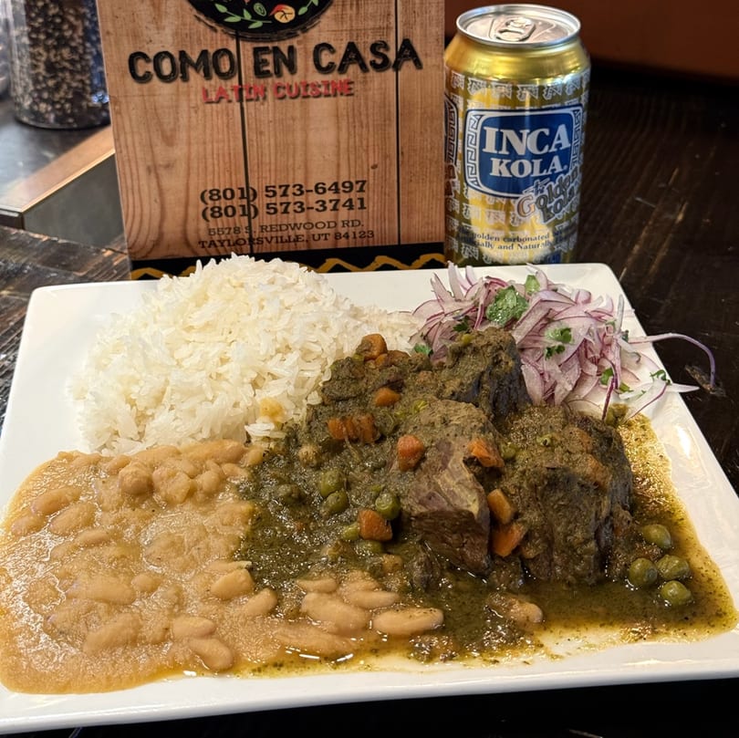 A plate of Colombian seco de res with rice, beans, and red onion salad, next to an Inca Kola can.